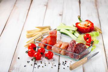 Products for a diet - raw meat of beef and chicken, a salmon and vegetables on a light wooden background. Selective focus.