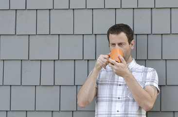 Man drinking from an orange mug with a gray background.
