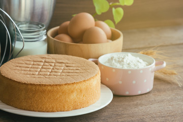 Homemade sponge cake on white plate.Soft and lite delicious sponge cake with ingredients: eggs flour milk on wood table. Homemade cake with ingredients in homemade bakery concept for bakery background