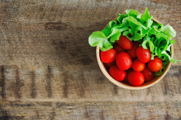 Fresh tomato and lettuce in wood bowl put on wood table. Top view or flat lay of tomato and green oak lettuce with copy space for background. Fresh green oak lettuce and tomato prepare for cooking.