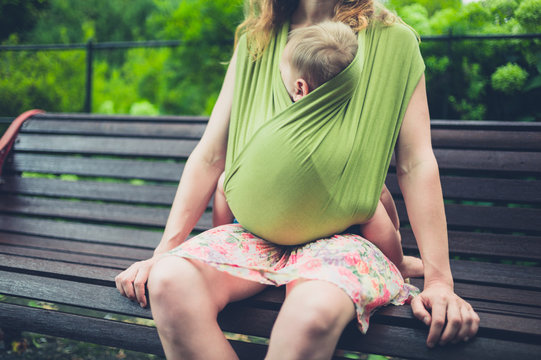 Mother with baby in sling resting on park bench