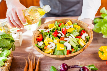 Obraz na płótnie Canvas man pouring olive oil into healthy salad on kitchen