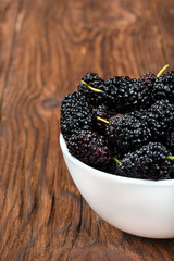 Part of bowl of fresh black mulberries on a wooden background, closeup