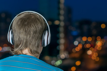 Man listening to music in big headphones against the background of a night city