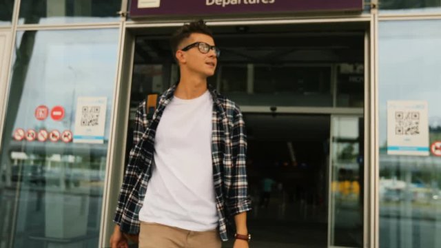 Young handsome man in the glasses with the baggage walking from the door of modern airport terminal to his home. Dolly shot.