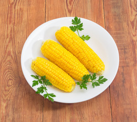 Boiled sweet corn on white dish on wooden surface