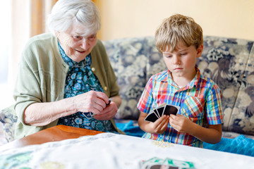 Active little preschool kid boy and grand grandmother playing card game together at home
