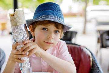 Cute healthy preschool kid boy eats turkish kebab sitting in cafe outdoors