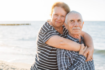 Happy family of two mature people hugging outdoors. Senior smiling couple standing on beach near sea on sunset.