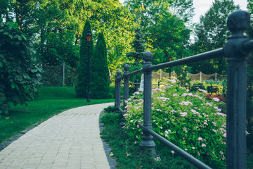 empty summer park with sidewalk and metal fence