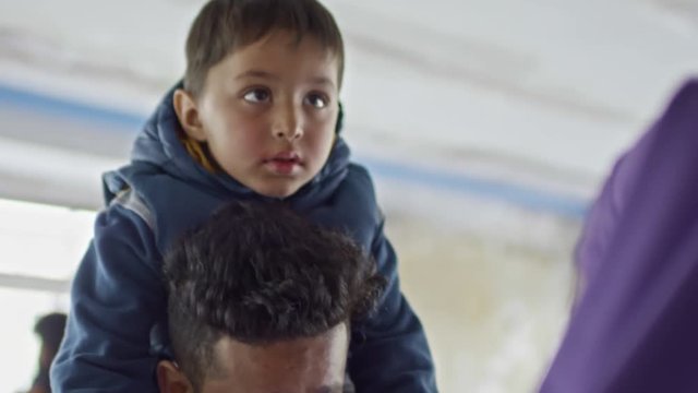 Tilt down with close up of little boy sitting on shoulders of young Arab man talking to unrecognizable woman in purple niqab