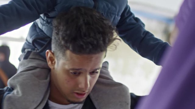 Tilt up of young Arab man holding little boy on shoulders and chatting with unrecognizable woman in purple niqab