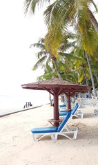 White wooden beach chairs with blue cushion and wood shades on the beach