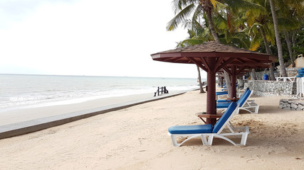 White wooden beach chairs with blue cushion and wood shades on the beach