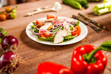 Fresh salad with chicken, tomato and greens on wooden background top view. Healthy food.