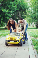 Parents helping daughter ride on kids toy car. Family having fun playing in the Park