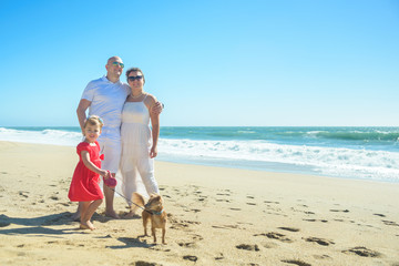 Young family with girl in red dress and dog on the beach