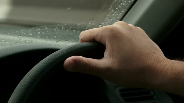 Driving on highway, rain. Detail of two Hands on the steering wheel, windshield POV. Right side wheel / driving - UK 