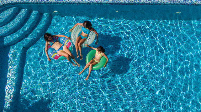 Aerial top view of family in swimming pool from above, mother and kids swim and have fun in water on family vacation in hotel resort
