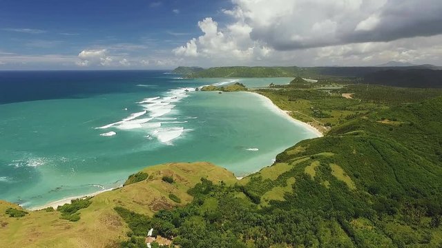 Aerial view of long Kuta Mandalika beach with white sand and turquoise water surrounded by green hills. Shot with drone on sunny day with blue sky in Lombok, Indonesia, fly forward.
