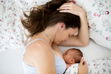 Young mother breastfeeds her baby, holding him in her arms and smiling