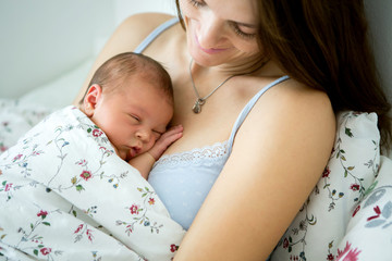 Young mother lying in bed with her newborn baby boy