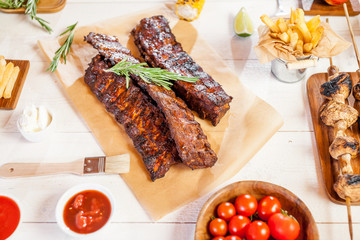 Spicy hot grilled spare ribs from a summer BBQ served with chips, corn and fresh tomatoes on an old wooden cutting board