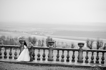 Fantastic wedding couple standing on the terrace with a view of a surrounding countryside. Black and white photo.