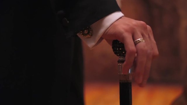 Gentleman holds a cane, a man fingering his fingers on the handle of a walking stick.
