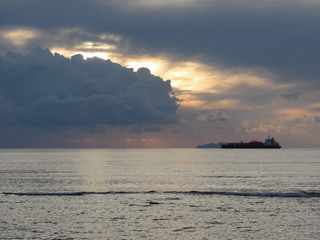 Naklejka premium Warm sea sunset with cargo ship at the horizon . Giants cumulonimbus clouds are in the sky. Tuscany, Italy