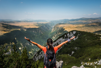 Hiker woman spreading her hands in front of huge river canyon. National Park Durmitor, Montenegro. - obrazy, fototapety, plakaty