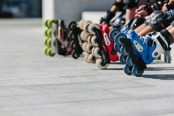 Feet of rollerbladers wearing inline roller skates sitting in outdoor skate park, Close up view of wheels befor skating - obrazy, fototapety, plakaty