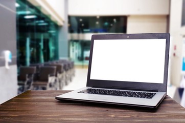 Fototapeta premium Laptop computer with white blank screen for advertising on wooden desk with blurred view of empty wheelchair in hospital, health care medical technology, working outside office, social media concept
