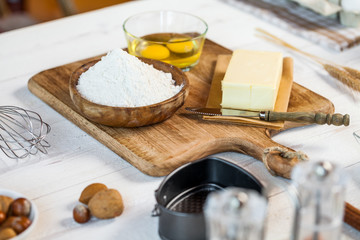 Baking ingredients in rural kitchen - dough recipe ingredients (eggs, flour, milk, butter, sugar) and rolling pin on wooden white table.