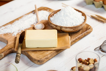 Baking ingredients in rural kitchen - dough recipe ingredients (eggs, flour, milk, butter, sugar) and rolling pin on wooden white table.