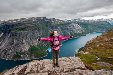 Young hiker girl with backpack enjoying valley view from top of a mountain with open arms. High resolution panorama, Norway. Troltunga route