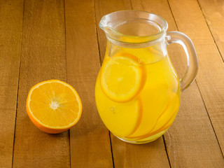 Lemonade from oranges in a glass pitcher and mugs on a wooden table.