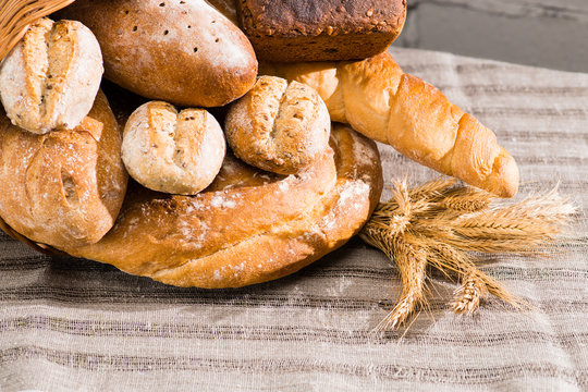 close-up various types of fresh bread in a basket on a table, brick background. Rustic style