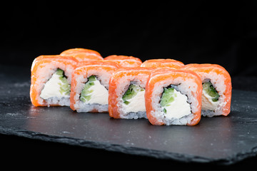 Traditional Japanese cuisine. Philadelphia sushi rolls with salmon, cream cheese, rice and cucumber on dark background, selective focus