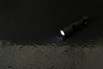 Flashlight water resistant in drops and a beam of light in darkness with copy space , A modern LED...