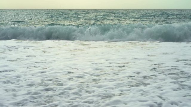 Waves washing the pebble beach. Waves lapping agains a shingle beach and cover it with white foam. Waves crashing into rocks.
