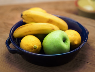 Bananas lemons and a green apple in a bowl.