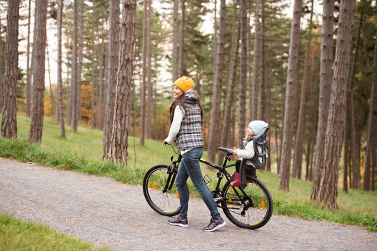 Young mother and daughter on bicycle in autumn park