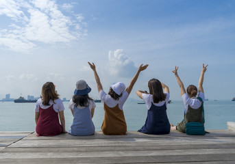 Group of five happy girls sit on wooden pier looking to the sea  vacations concept