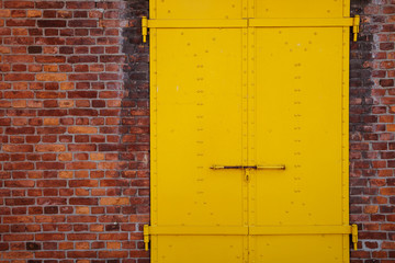 Yellow painted metal door and brick wall background