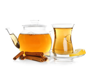 Glass teapot and cup with aromatic hot cinnamon tea on white background