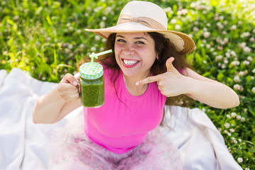 Young happy woman shows on green smoothies at a picnic. Healthy food, detox and diet concept