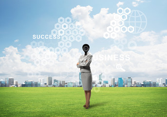 Camera headed woman standing on green grass against modern cityscape