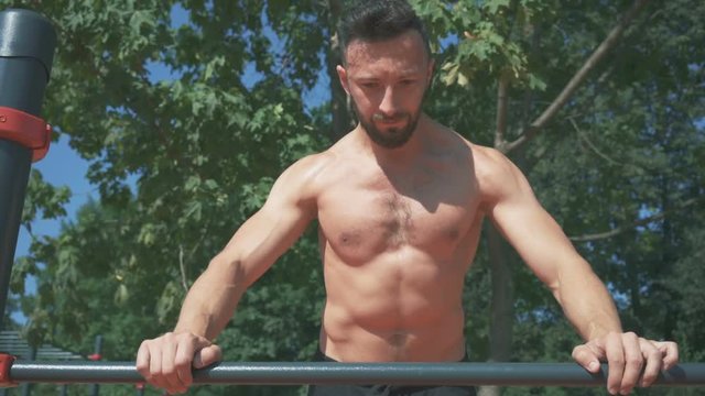 Muscular athlete exercising push up outside in park.