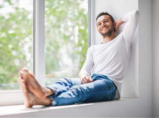 Handsome smiling man relaxing on window sill